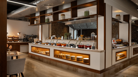 A brightly lit, upscale restaurant buffet area featuring wooden panelling and modern food display counters.