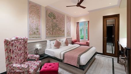 A spacious bedroom at Panna Vilas Palace, complete with a wooden table, cushioned furniture, warm lighting, and a large window