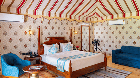 King size bed with seating area and patterned wall decor in the Luxury Tent with Jacuzzi at Pushkara Resort & Spa, Ajmer