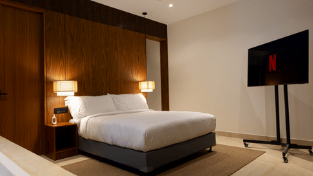 Hotel room at SUKAVI with a large bed, wooden paneling on the walls, and a wall-mounted television.