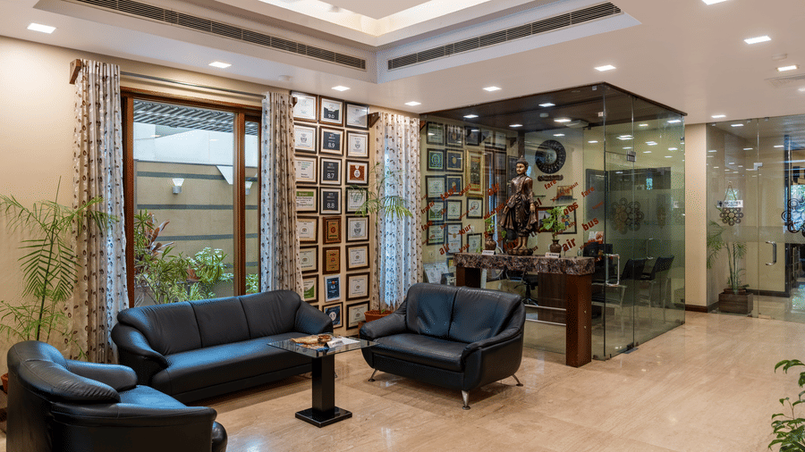 A stylish hotel lobby view featuring sleek black leather sofas, polished marble flooring, along with several indoor plants and a false ceiling above- Amantra Comfort Hotel