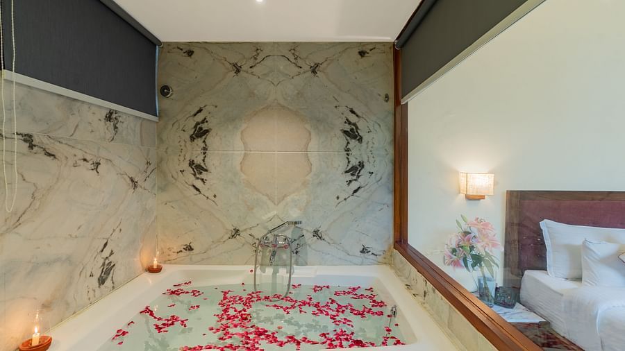 close up image of the bathtub with candles in the corner and a glass partition between the room and the bathroom in the luxury bathtub villa in aranya vilas