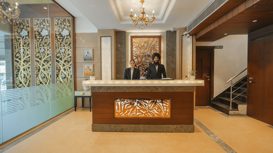 A wider view of the ornate hotel reception area, showing the decorative desk, a staff member, and luxurious wall panels at BluSalzz Select City Centre, Amritsar.