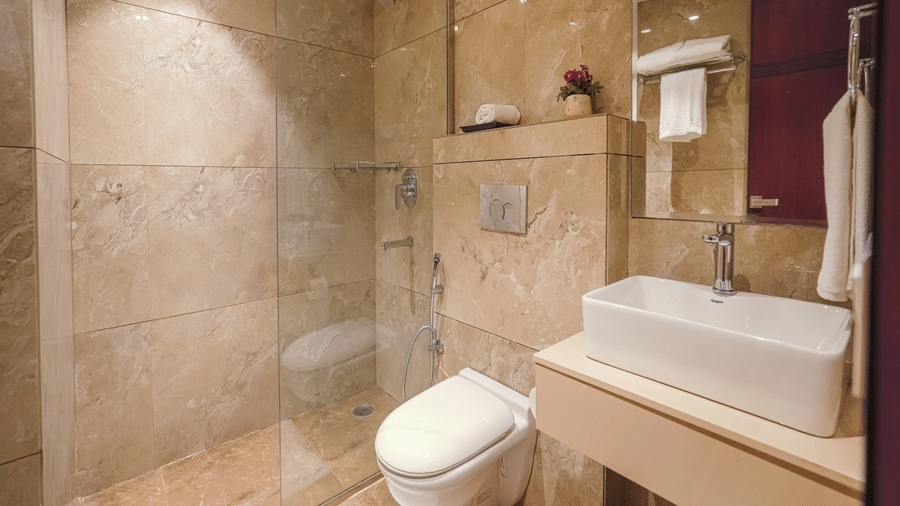 A hotel bathroom featuring marble-effect tiling, a toilet, a square basin, and a glass partition for the shower area at BluSalzz Select City Centre, Amritsar.