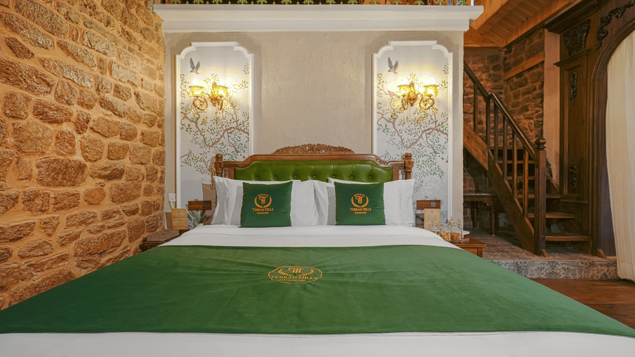 The executive-suite at BluSalzz Terrah Hills Resort, Dalhousie, bedroom with a bed featuring a duvet, a headboard, wall mounted light fixtures, brick walls, and wooden flooring.