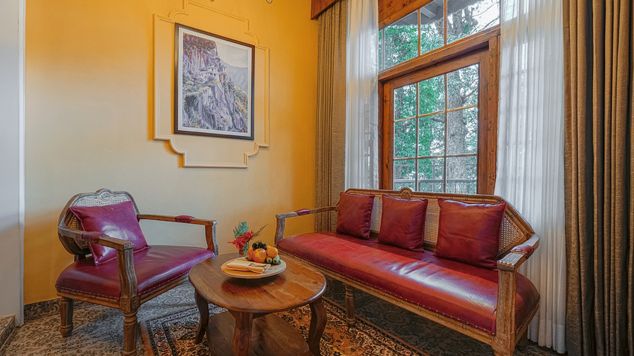 A seating area in a premium room at BluSalzz Terrah Hills Resort, Dalhousie, with exposed stone walls and arched ceilings, featuring a sofa, chairs, and a wooden coffee table. 