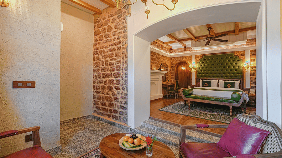The premium room at BluSalzz Terrah Hills Resort, Dalhousie, with stone archways, a bed visible in the background, chairs, and a wooden table in the foreground.