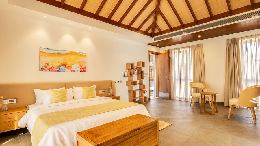 A cosy bedroom with a pitched wooden ceiling, a king-sized bed, soft yellow accents, and natural light filling the space - BluSalzz Villas - Alocassia, Anjuna