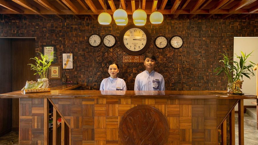 A reception area with two friendly staff members behind a wooden desk, decorated with plants and soft lighting. The space is welcoming and stylish with natural materials - Coral Reef Resort & Spa, Havelock