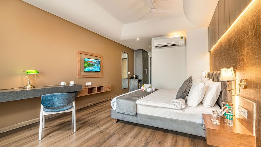 An image of the deluxe room with a bed, work desk and chair, flat screen TV, and warm lighting - DLS Ganga Bliss, Haridwar