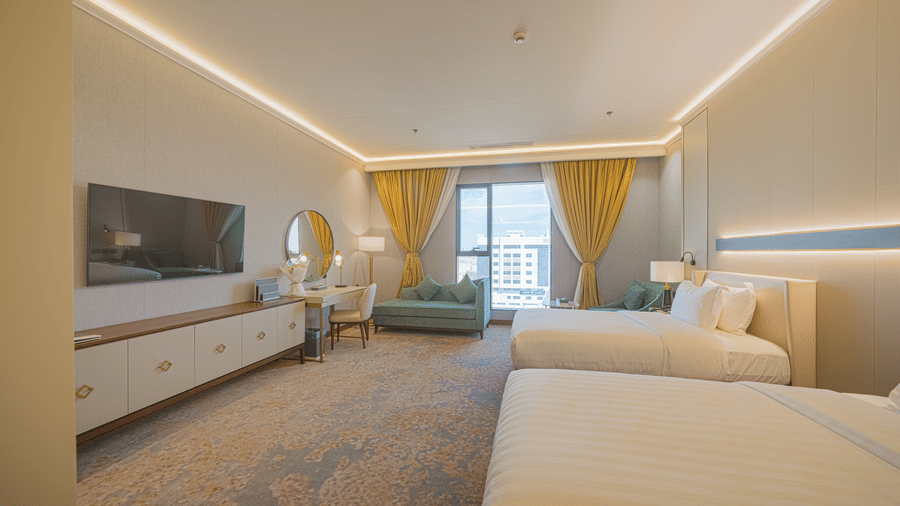 Drawn curtains offering views of the hills beyond the glass windows in the Deluxe Twin Room at Grand Iva Hotel, Abha.