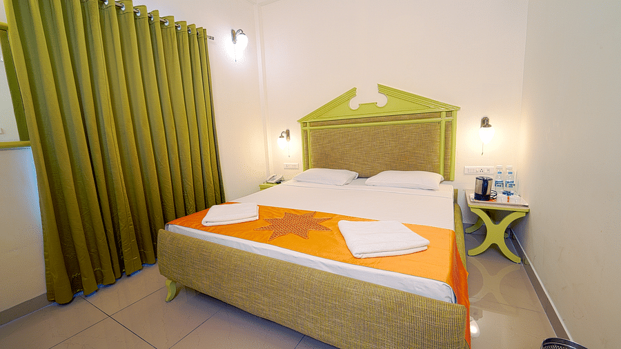 A hotel bedroom with a large double bed, green headboard, and green curtains, giving a cozy ambience at Greens Inn - Best Accommodation in Ramoji Film City.