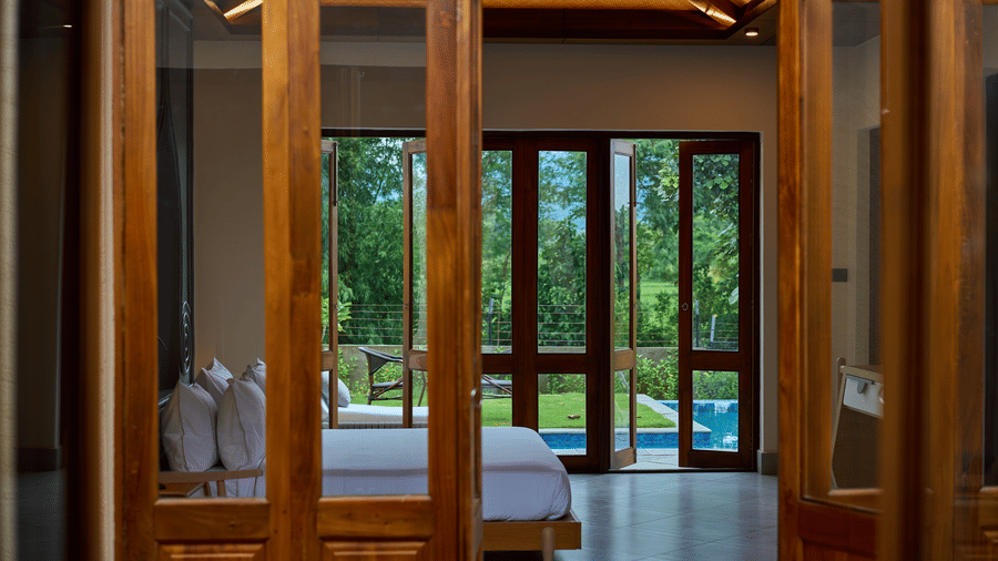 Open wooden doors featuring a bedroom and a private swimming pool outside at Hotel Sonar Bangla, Ajodhya Hills.