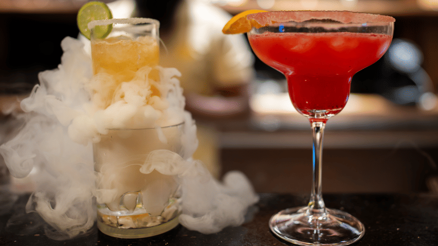 A bar counter featuring a smoking cocktail and a red cocktail at Hotel Sonar Bangla, Ajodhya Hills.