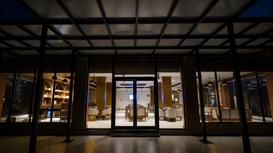 A lit building exterior at night featuring large windows and a covered patio at Hotel Sonar Bangla, Ajodhya Hills.