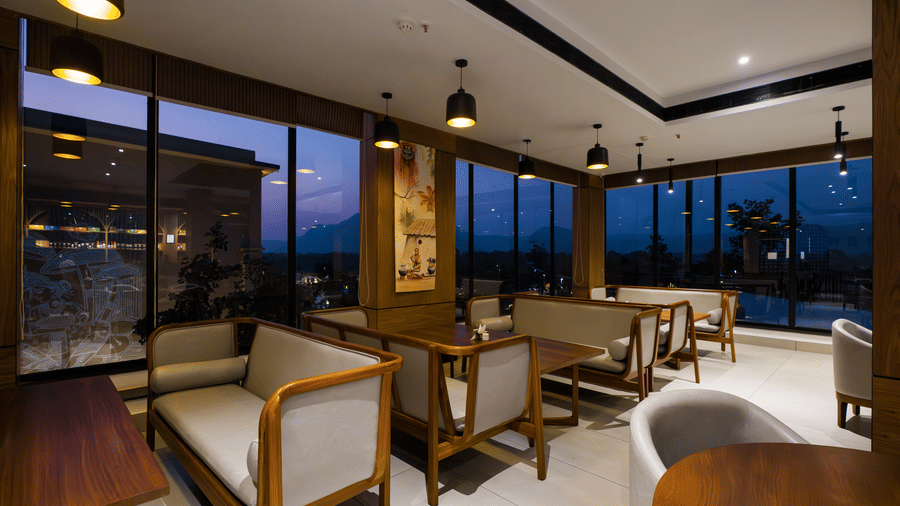 A restaurant interior featuring wooden tables, seating, and large windows looking outside at Hotel Sonar Bangla, Ajodhya Hills.