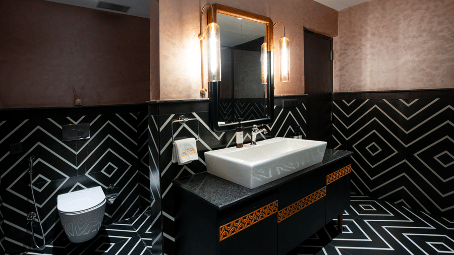 A stylish bathroom vanity area featuring geometric black wall patterns, a modern wash basin, illuminated mirror, and premium fittings | Hotel Sonar Bangla, Susunia