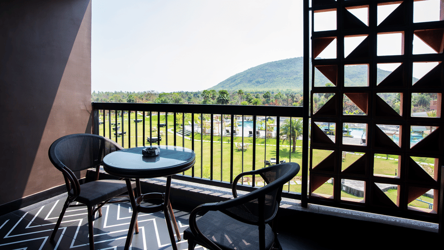 The private balcony seating area attached to the Super Deluxe Room overlooking scenic greenery and distant hill views through decorative lattice walls | Hotel Sonar Bangla, Susunia