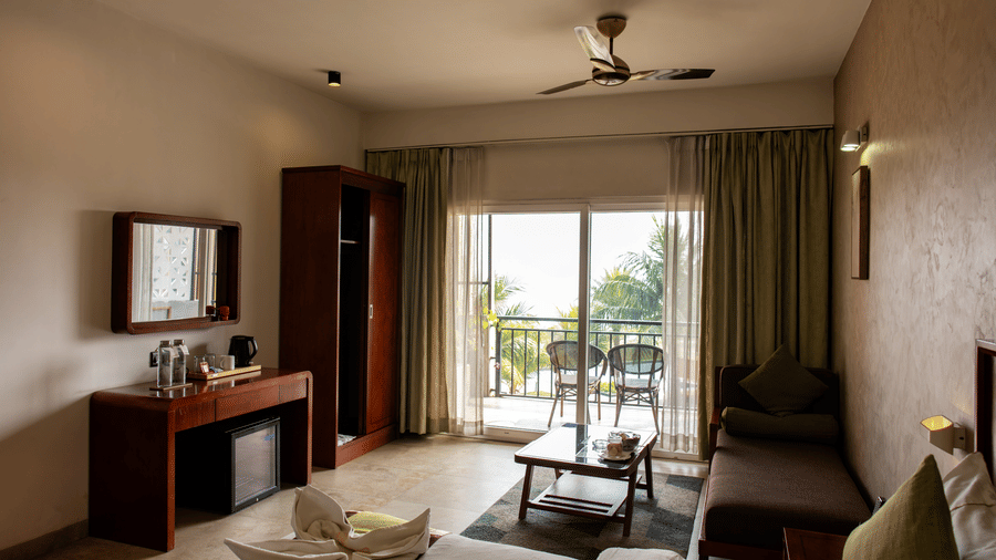 A Deluxe Room featuring a bed, wardrobe, a table, and open curtains displaying the balcony at Hotel Sonar Bangla, Taki.