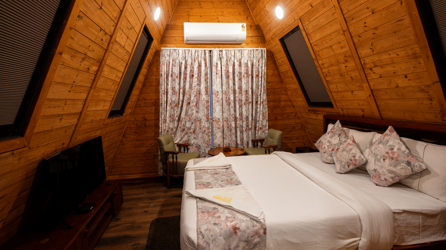 Duplex villa double bedroom with dark wooden sloped ceiling and cushioned bed at Hotel Sonar Bangla, Taki.