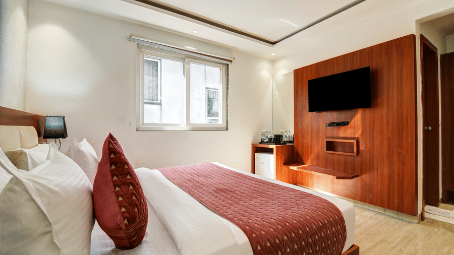 Bright hotel room featuring a wall-mounted TV, wooden cabinetry, and natural window lighting - Hotel Velocity