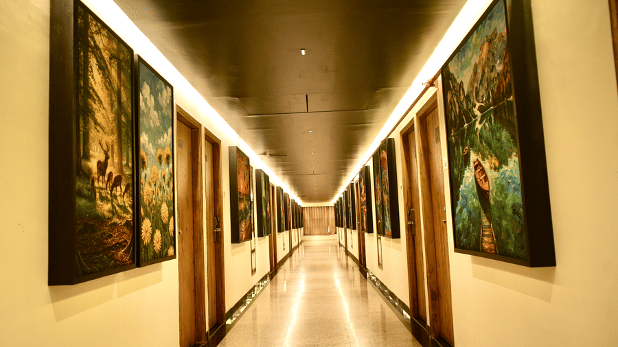 A hallway at Infiniti Hotel, Indore featuring framed artwork on both walls, recessed ceiling lights, and wooden doors.