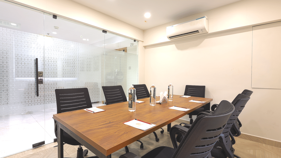 A boardroom at Lemonridge by Monday Hotels - KPHB featuring a long wooden conference table, black ergonomic mesh chairs, a white wall board, and a ceiling AC unit.