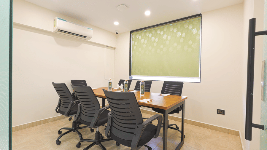 A meeting room at Lemonridge by Monday Hotels - KPHB featuring a wooden table, office rolling chairs, and a wall air-conditioner.