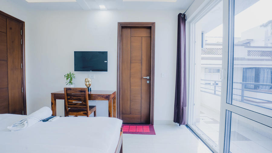 Bedroom of Lime Tree Hotels & Service Apartment Private Limited featuring a study table, a chair, and a balcony with glass doors.