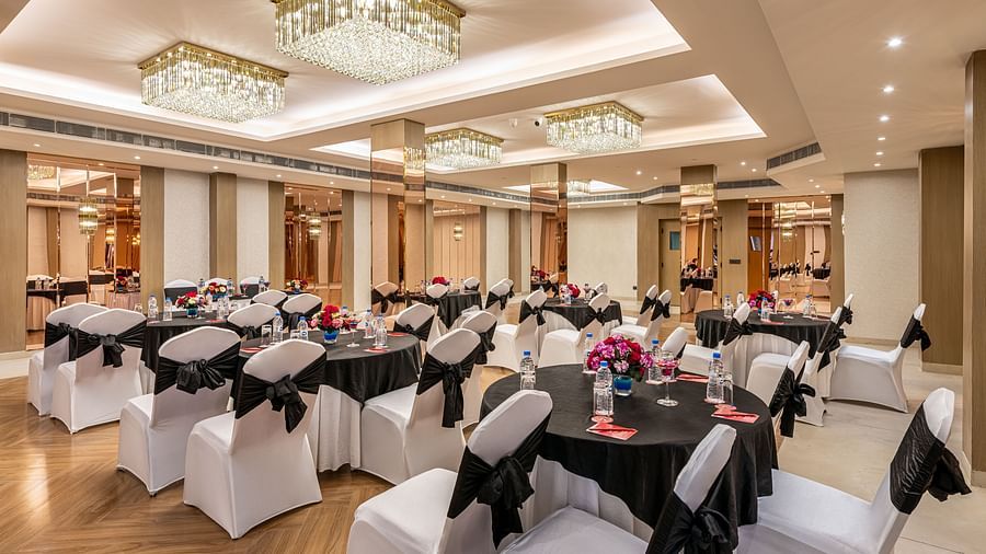 Event space with round tables and white chairs adorned with black fabric, ready for a banquet or gathering. Features a decorative ceiling with hanging lights and mirrored wall accents - Lords Eco Inn Dehradun.