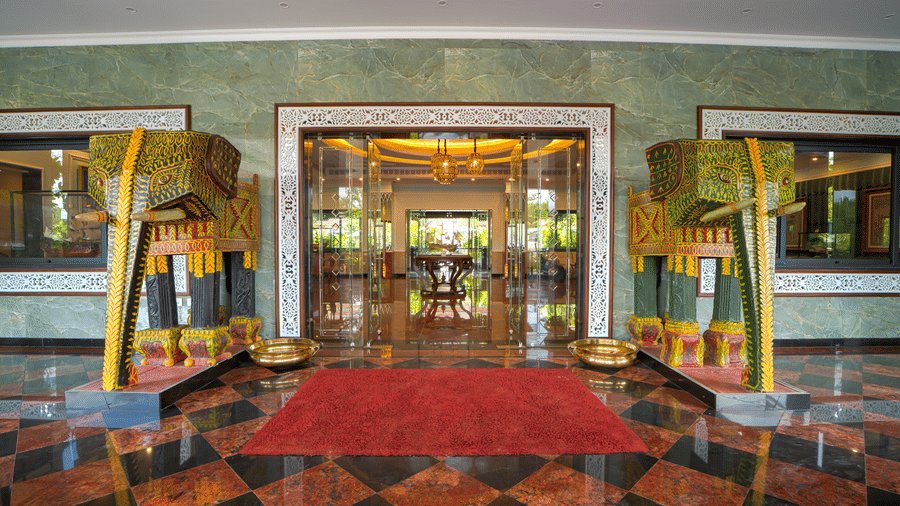 A grand entrance lobby with polished flooring, red carpet, ornate pillars, large glass doors with golden accents at MAYFAIR Bay Resort, Paradeep.
