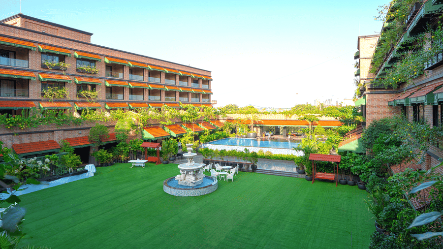 Outdoor lawn with pathways, seating areas, fountain, greenery, and multi-storey building of MAYFAIR Bay Resort, Paradeep.