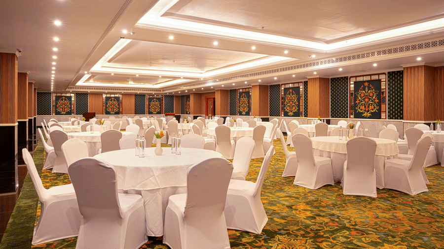 A large banquet hall set up with numerous circular tables draped in white cloths at MAYFAIR Bay Resort, Paradeep.