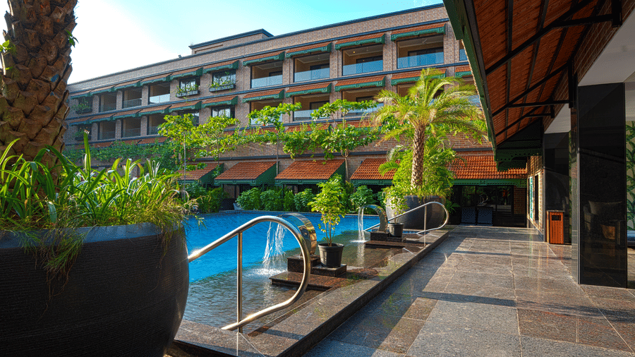 A poolside area featuring sun loungers, large potted plants, and a shimmering blue pool reflecting the sky at MAYFAIR Bay Resort, Paradeep.