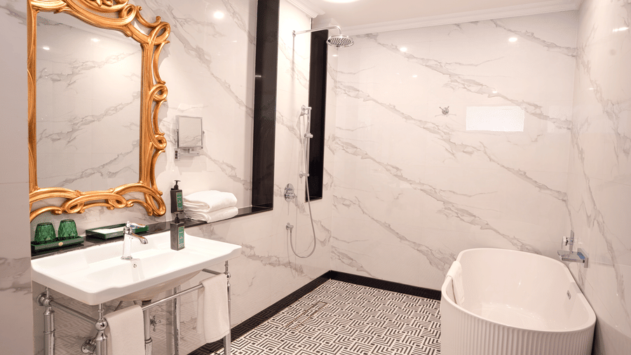 A modern bathroom featuring a freestanding bathtub, marble walls, a white sink, and a decorative gold-framed mirror at MAYFAIR Bay Resort, Paradeep.