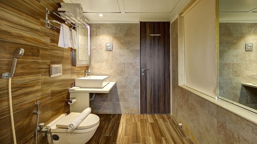 Bathroom with toilet, square basin, mirror, wooden and beige tiles, and a door.