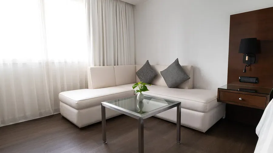 Elegant hotel seating area featuring cream sectional sofa, glass coffee table, grey cushions, and walnut entertainment unit with contemporary styling at Night Hotel Bangkok.