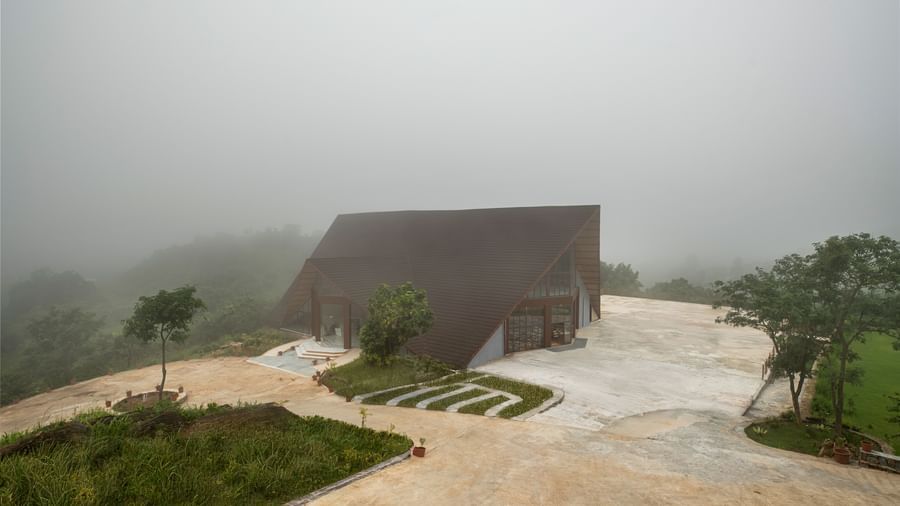 An elevated view of a building at the Osian Valley Resort & Spa, showing the entrance and surrounding paved area, with a separate building visible in the background, all enveloped in fog.