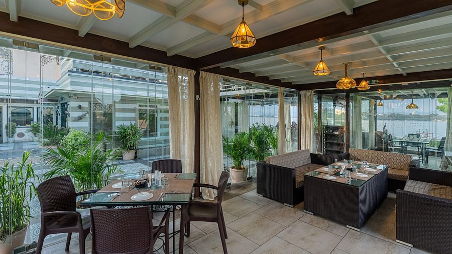 At Panna Vilas Palace, the restaurant area features a four-seater table with wooden chairs arranged around it, accented by warm lighting and potted plants | Panna Vilas Udaipur