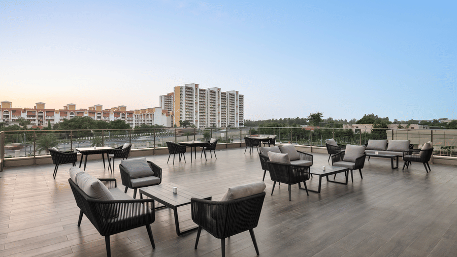 Outdoor rooftop terrace seating area at dusk, with grey lounge chairs, low tables, and a cityscape view under a clear blue sky.