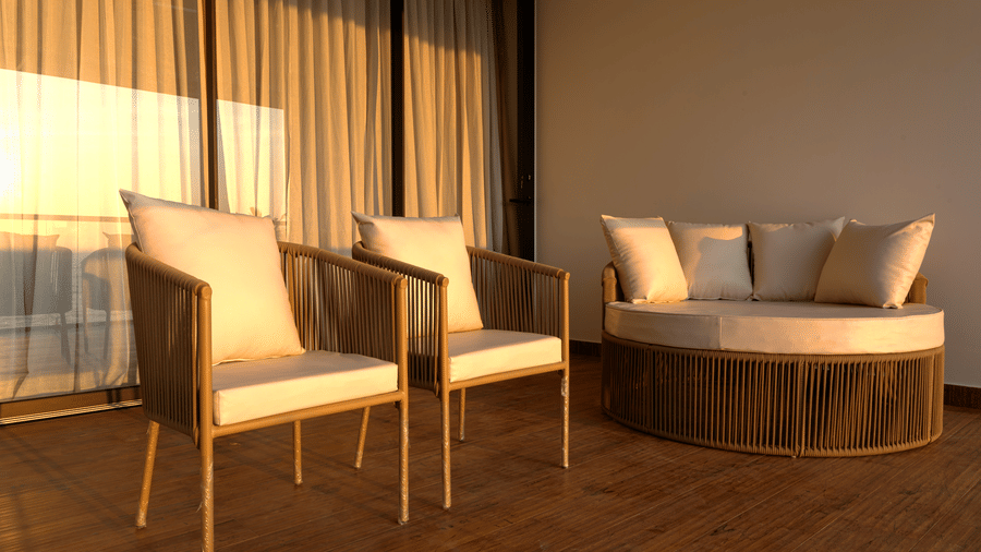 Indoor seating area at SUKAVI with 2 wooden-framed armchairs, a round sofa, and natural light coming through nearby windows.