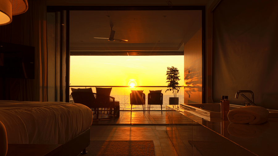 Hotel room at SUKAVI through large sliding doors onto a balcony at sunset, showing outdoor chairs, a table.