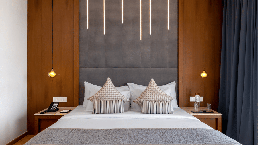 A symmetrical view of a king size bed flanked by bedside tables and hanging pendant lights against a feature wall at Tiara by MPS.