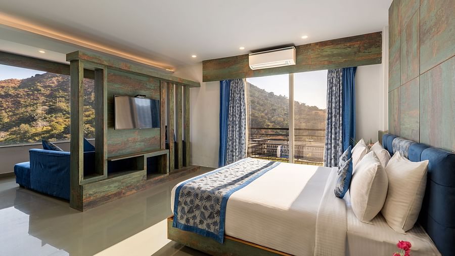 A bedroom with a made bed, patterned runner and a mountain view through the window - Via Lakhela Resort & Spa 