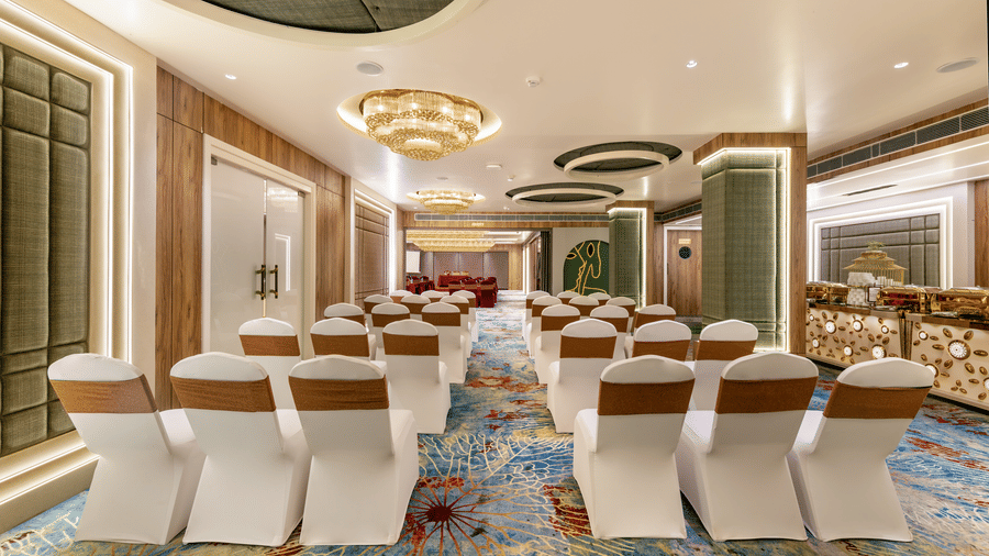 Banquet hall at Lords Inn Sangam, Bhopal featuring rows of white and gold chairs arranged with a center aisle, elegant lighting, and patterned carpet flooring.