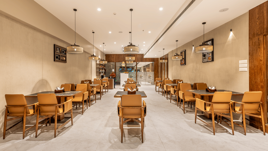 Banck-angle view of L Café showing modern wooden tables surrounded by mustard-yellow chairs, set in a bright, contemporary interior with recessed lighting – Skkylight Lords Inn, Nanded