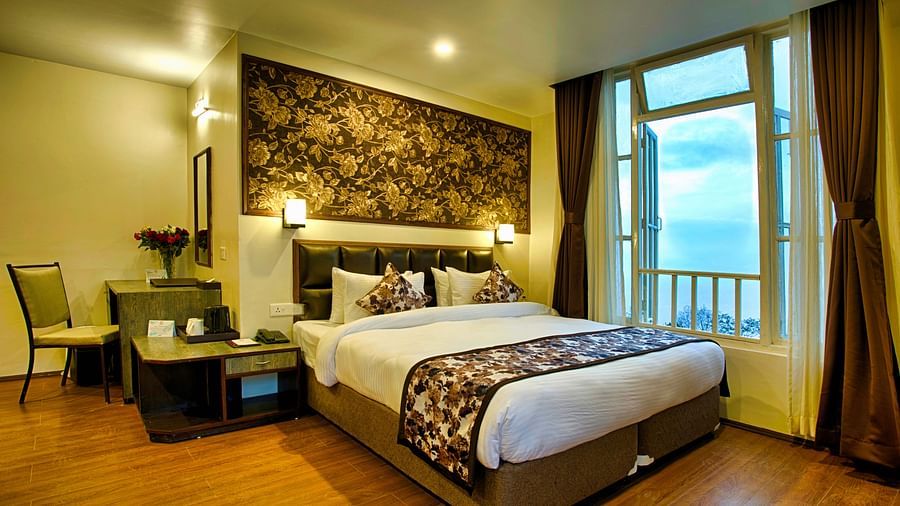 a lavish bedroom with wide open windows along with a workdesk and chair, tea & coffee maker, a king size bed - the aryan regency