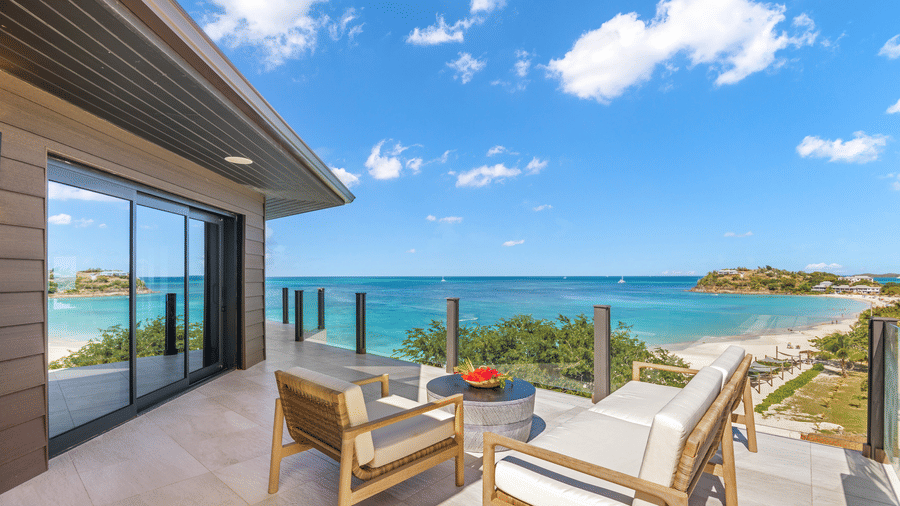 A balcony at the Tamarind Hills Resort and Villas, Antigua, with lounge chairs and a table with a view of the sea.