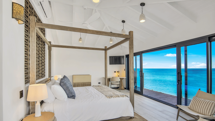 A bedroom at Tamarind Hills Resort and Villas, Antigua, with a canopy bed, panoramic sea views, and floor-to-ceiling glass windows.