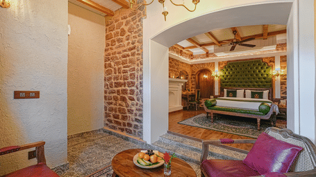 The premium room at BluSalzz Terrah Hills Resort, Dalhousie, with stone archways, a bed visible in the background, chairs, and a wooden table in the foreground.